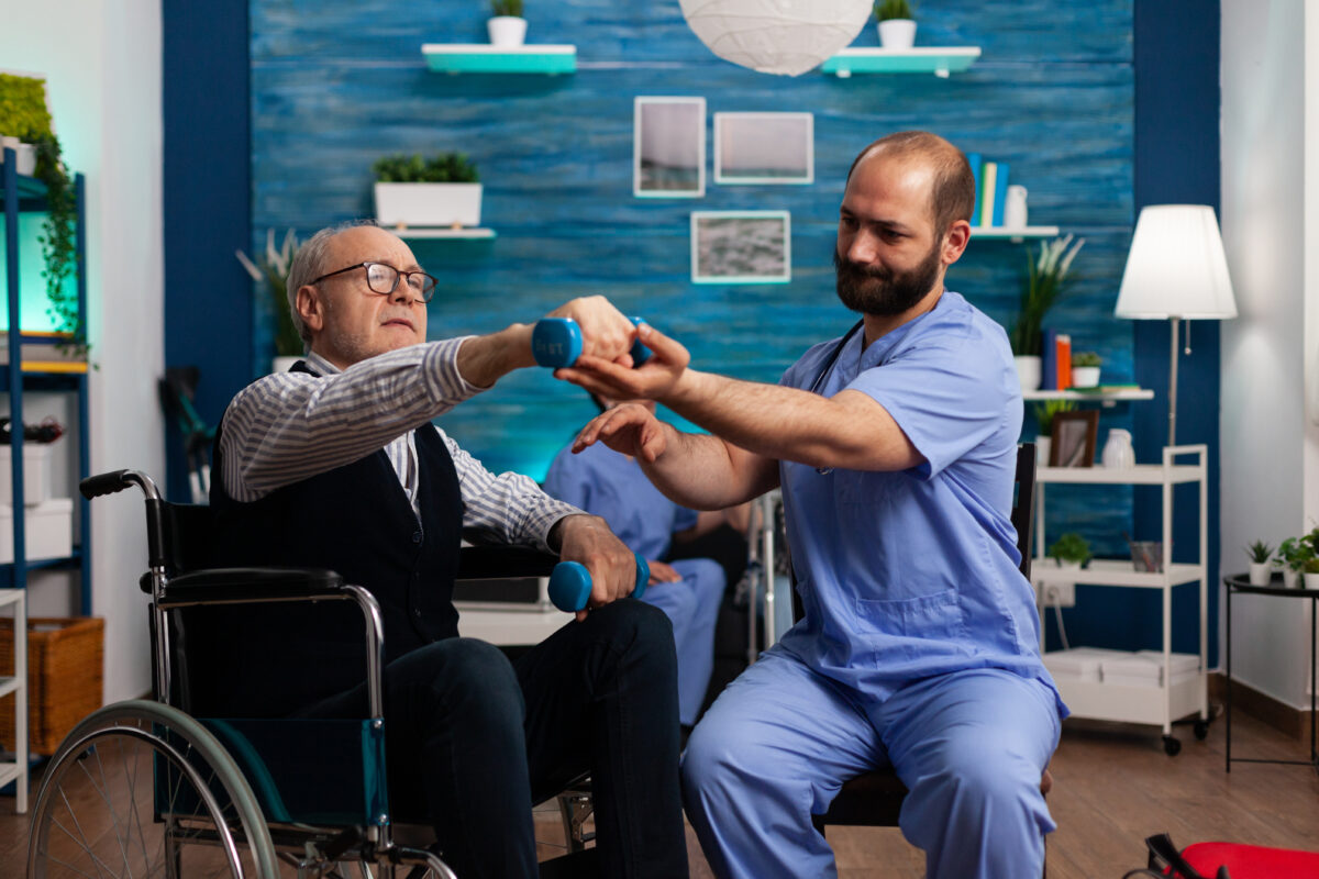 Orthopedic doctor assisting senior male patient in wheelchair with physiotherapy at top hospital in India