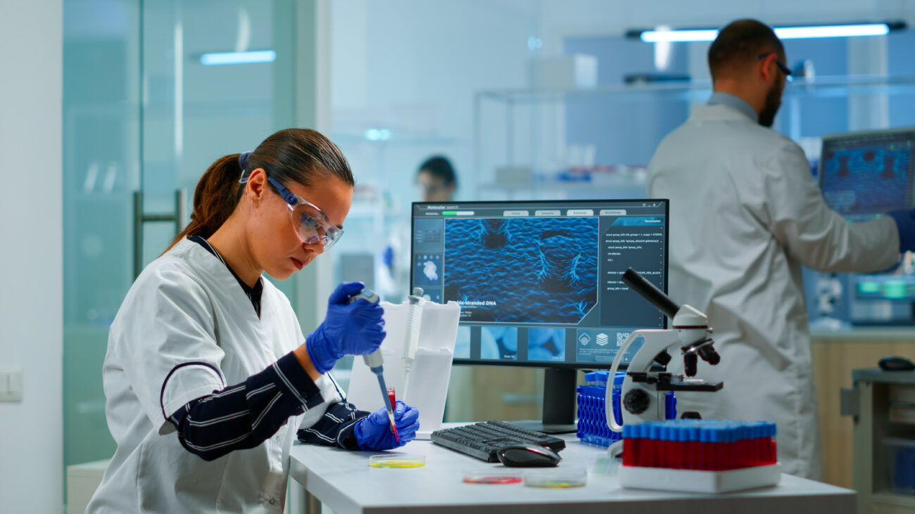 Female researcher conducting lab experiment during biomedical research for clinical trials in India, with advanced molecular analysis displayed on screen.
