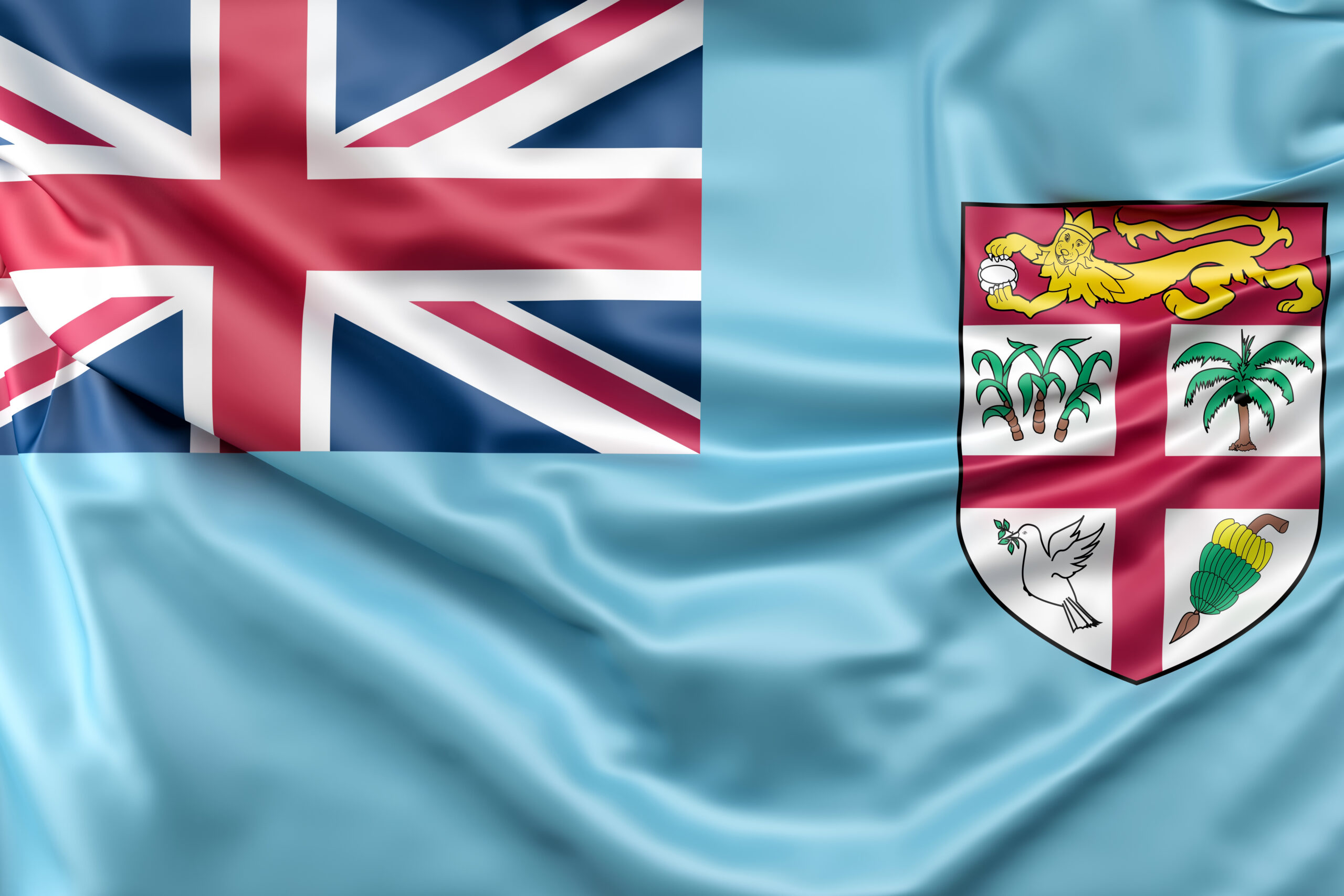 The national flag of Fiji, featuring a light blue field with the Union Jack in the upper left corner and a shield with a golden lion and native symbols on the right. The fabric of the flag appears slightly rippled.