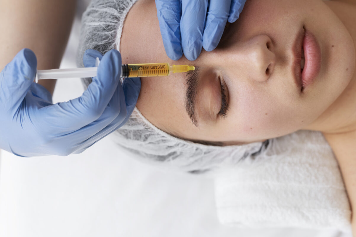 A close-up of a woman receiving a Platelet-Rich Plasma (PRP) therapy injection into the skin near her eyebrow. She is lying relaxed with her eyes closed while a healthcare professional in blue gloves administers the treatment.